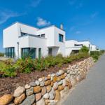 Moderne weiße Villa mit Steinmauer und Blumenbeet am Wasser