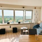 Wohnzimmer mit großem Fenster und Blick auf die Stadt. Sofa, Tische und Holzboden.