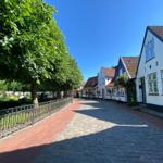 Kurze Straße mit gepflastertem Weg und historischen Häusern mit weißen Fassaden.