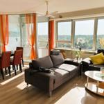 Wohn- und Essbereich mit Sofa, Tisch und großen Fenstern. Blick auf grüne Landschaft.