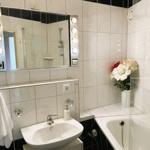 Badezimmer mit Waschbecken, Dusche und Badewanne. Spiegel mit Beleuchtung und Blumen auf dem Rand.