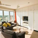 Wohnzimmer mit Sofa, Couchtisch und TV-Einbauwand. Große Fenster mit Blick auf Wasser.