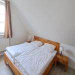 Schlafzimmer mit Doppelbett, Nachttisch und Kleiderschrank. Fenster mit Vorhängen.