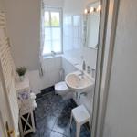 Badezimmer mit Toilette, Waschbecken und Fenster. Weiße Fliesen und Duschwanne.