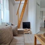 Wohnzimmer mit Sofa, TV und Holztreppe. Küche im Hintergrund.