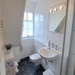 Badezimmer mit Waschbecken, Toilette und Dusche. Fenster, Spiegel und Handtuchheizung sichtbar.