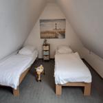 Zwei Einzelbetten in einem Dachzimmer mit Wandbild und Kinderwagen.