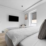 Schlafzimmer mit Bett, Fernseher und Fenster. Holzboden und weiße Wände.