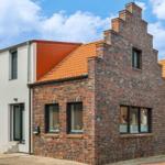 Haus mit Backsteinfassade und rotem Dach unter blauem Himmel.