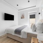 Schlafzimmer mit Bett, Fernseher und Tür zum Balkon.