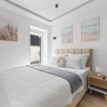 Schlafzimmer mit Bett, Nachttisch und Wandbildern. Tür führt nach draußen.