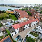 Häuser mit roten Dächern am Wasser, Marina im Hintergrund.