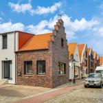 Reihenhaus mit rotem Dach und Backsteinfassade an einer Straße mit Kopfsteinpflaster.