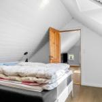 Schlafzimmer mit Dachschrägen, Bett und Tür zu einem weiteren Raum.