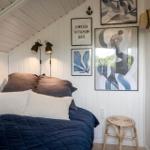 Schlafzimmer mit Bett, Wandbildern und Stehlampe.