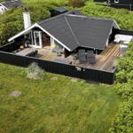 Modernes Haus mit großem Holzterrasse, Grill und Außensitzgelegenheiten.