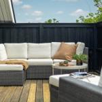 Terrasse mit Rattanmöbeln, Kissen und Tisch. Holzdecke und schwarzer Zaun.