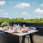 Terrasse mit Tisch und Stühlen, gedeckt mit Obst und Getränken, Blick auf grüne Vegetation.