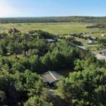 Aerial view of a campground with cabins, trees, and open fields under clear skies.