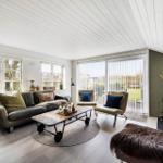 Wohnzimmer mit Sofa, Sesseln, Kamin und großen Fenstern.