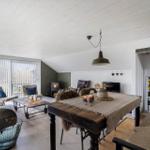 Wohn- und Essbereich mit Holztisch, Sofa und Kaminofen. Weiße Decke und Holzboden.