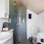 Badezimmer mit Dusche, Waschmaschine und Toilette unter Holzdecke.