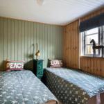 Zwei Betten mit gemusterten Decken, grüne Wand, Holzwände und Fenster mit Pferdfigur.
