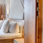Bedroom with bed, pillows, and nightstand. Background with dried plants and wall decor.