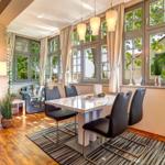 Esszimmer mit Tisch, Stühlen und großen Fenstern. Holzboden und Vorhänge.