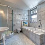 Bad mit Badewanne, Dusche, Waschbecken und Toilette. Fenster mit buntem Glas.