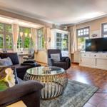 Wohnzimmer mit Sofa, Sessel, Glas-Tisch und TV. Holzboden und große Fenster.