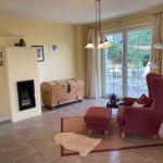 Wohnzimmer mit Sessel, Kamin und Terrasse. Holztruhe und Beleuchtung.