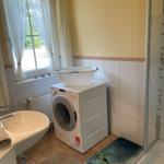 Badezimmer mit Waschmaschine, Dusche und Fenster mit Vorhängen.