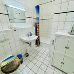 Badezimmer mit Badewanne, Waschbecken und WC. Weiße Fliesen und Schrank.