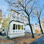 Modernes Haus mit Balkon und Treppenaufgang. Umgeben von Bäumen und Herbstlaub.