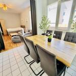 Essbereich mit Holztisch und Stühlen. Im Hintergrund Schlafzimmer mit Bett und Sofa.