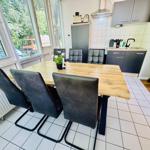 Essbereich mit Holztisch, vier Stühlen und Küchenzeile im Hintergrund.