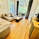 Wohnung mit Schlafzimmer, Wohnbereich und Essplatz. Holzboden und große Fenster.