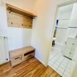 Flur mit Holzbank und Garderobe. Blick in die weiße Badewanne.
