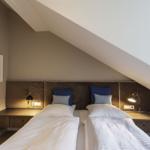 Zwei Einzelbetten unter Dachschräge mit Nachttisch und Wandbild.