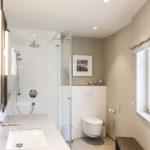 Badezimmer mit Dusche, Waschbecken und Toilette. Fenster mit Rollladen.