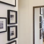 Wand mit schwarz gerahmten Bildern und Spiegel, der Wohnbereich reflektiert.