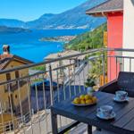 Terrasse mit Tisch, Stühlen und Blick auf See und Berge.
