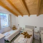 Zimmer mit drei Betten, Holzdecke und Fenster mit Blick auf Steinwand.