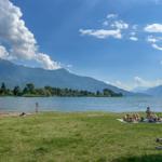 Grüner Strand mit Menschen, die sich sonnen, und Bergen im Hintergrund.