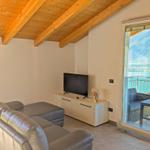 Wohnzimmer mit Sofa, Fernseher und Balkon mit Seeblick.