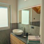 Badezimmer mit Waschtisch, Spiegel und Fenster. Holzdecke und gefaltete Handtücher.