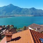 Panoramablick auf See und Berge mit roten Dächern im Vordergrund.
