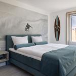 Schlafzimmer mit Surf-Motivwand, Bett und Fenster zum Balkon.