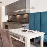 Essbereich mit Holztisch, blauer Sitzbank und moderner Küche im Hintergrund.